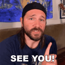 a man with long hair and a beard says " see you " with his finger