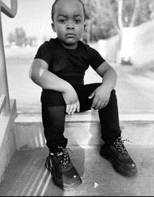 a black and white photo of a young boy wearing a black shirt and black pants