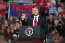 donald trump is giving a speech at a podium in front of a crowd at a rally .