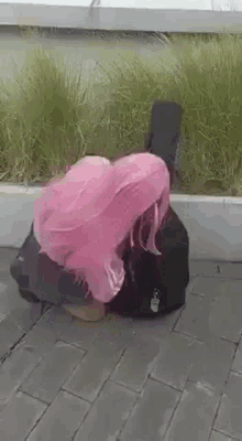 a woman with pink hair is kneeling down next to a guitar case on the sidewalk .