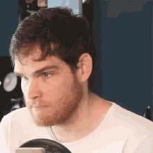 a man with a beard is wearing a white shirt and looking at his phone