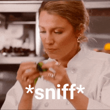 a woman in a chef 's coat sniffs something in a kitchen
