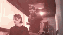 a man with a beard is standing next to another man with a gyro shirt on .