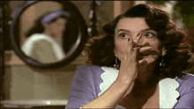 a woman covering her mouth with her hand while looking at herself in the mirror