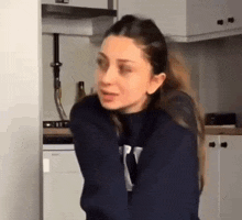 a woman in a blue sweater is standing in a kitchen with her arms outstretched .