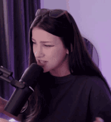 a woman wearing sunglasses and a black shirt is talking into a microphone .