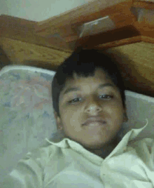 a young boy in a yellow shirt is laying on a bed and taking a selfie