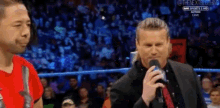 a man in a suit is talking into a microphone in front of a crowd