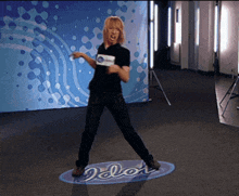 a woman in a black shirt is dancing in front of an idol sign