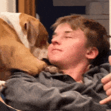 a young man is laying on a couch with a dog on his head