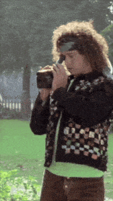 a man with curly hair is taking a picture with a camera in a park
