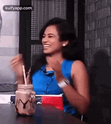 a woman is sitting at a table with a milkshake in a mason jar and laughing .