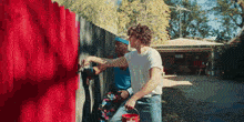two men are painting a fence with a red bucket