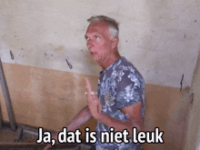 a man in a floral shirt stands in front of a wall with the words ja dat is niet leuk below him