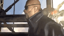 a bald man wearing sunglasses and a mask is standing in a room .
