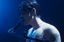 a shirtless man singing into a microphone with a blue background