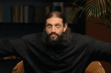 a man with long hair and a beard is raising his hands in the air