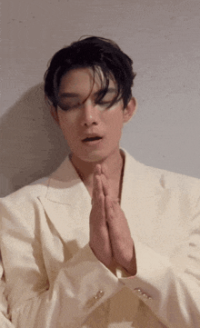 a man in a white suit is praying with his hands folded in front of his face