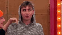 a man wearing a hoodie is being touched by another man in an orange hat .
