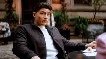 a man in a jacket is sitting at a table with a donut on it .