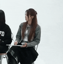 a girl wearing a sweatshirt that says fd sits in a chair with a notebook in her hand