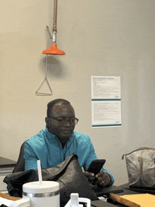a man sits at a desk looking at his phone with a sign on the wall that says ecgp on it