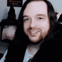 a man with long hair and a beard is smiling for the camera in front of a witch hat .