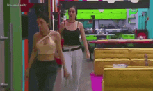 two women are walking in a room with the words universo reality on the bottom