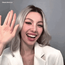 a woman in a white jacket is smiling and waving her hand .
