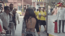 a woman in a backless top is walking down a street with a star plus logo in the background