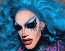 a close up of a drag queen 's face with blue hair and black eye shadow