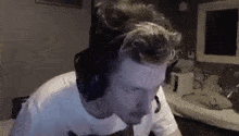 a man wearing headphones and a white shirt is sitting in front of a computer screen .