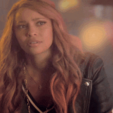 a woman with long red hair wears a black leather jacket