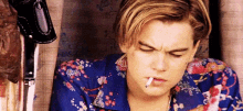 a young man is smoking a cigarette and wearing a blue shirt .