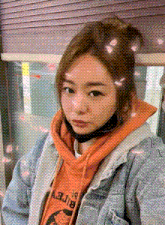 a woman wearing an orange hoodie and a denim jacket taking a selfie