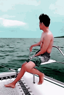 a shirtless man is sitting on a boat in the water