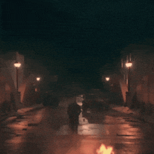 a man walking down a street at night with cars parked on the side