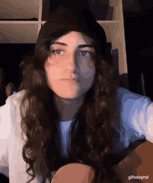 a woman with long hair and a nose ring is wearing a black beanie and a white shirt .