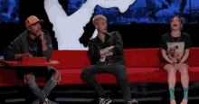 three people are sitting on a red couch and one has a shirt that says walk