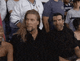 two men are sitting in a crowd of people at a wrestling event .