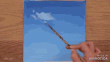 a person is painting a blue sky with white clouds with a brush