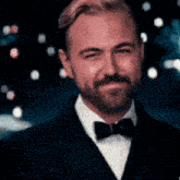 a man with a beard is wearing a black suit and bow tie