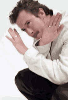 a man in a white shirt and black pants is squatting down with his hands outstretched .