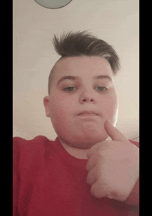 a young boy in a red shirt is giving a thumbs up sign