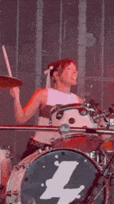 a woman is playing drums with a drum with the letter l on the front