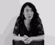 a woman is sitting in a chair with her hands folded in front of her .
