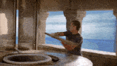 a man in a blue shirt is standing in front of a large window overlooking the ocean