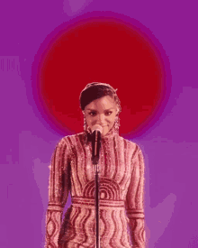 a woman in a red dress is singing into a microphone on a purple background .