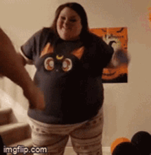 a woman wearing a cat t-shirt is dancing in front of a halloween poster