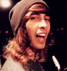 a young man with long hair wearing a beanie and a gray sweater